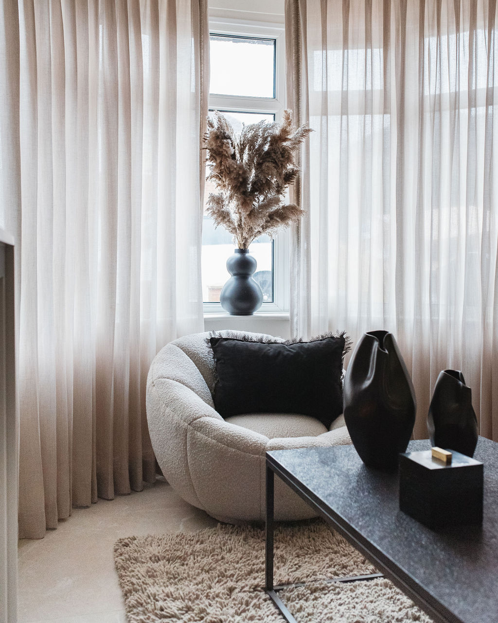 a cream chair with neutral sheer curtains at the windows